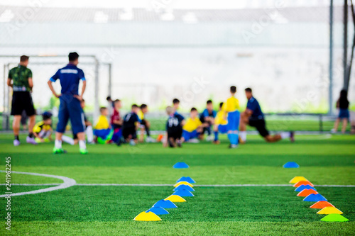 Cone markers is soccer training equipment on green artificial turf with blurry kid players training background