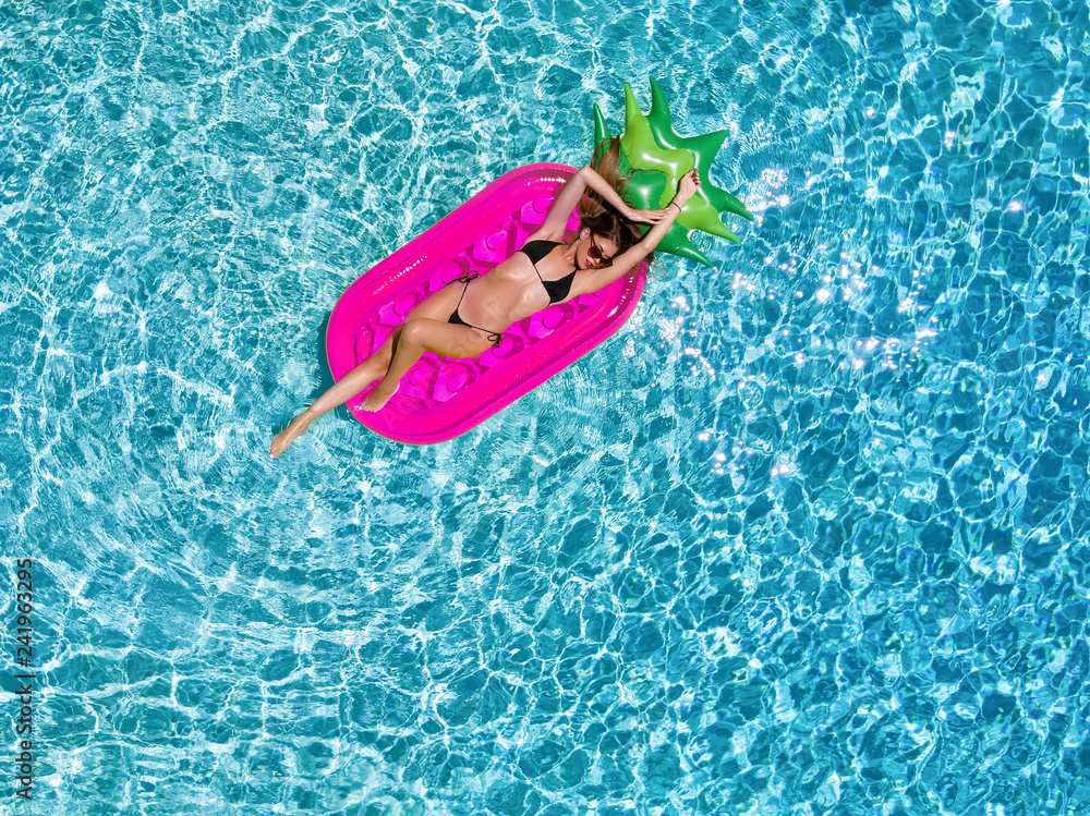 Sportliche, junge Frau im Bikini entspannt auf einer Luftmatratze im Pool an einem heißem Sommertag