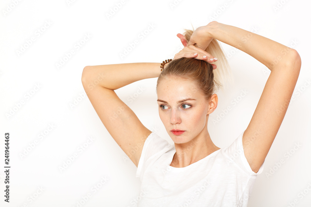 A young, thoughtful lady brushed her blond long hair back to gather it in a bun. A young, thoughtful lady brushed her blond long hair back to gather it in a bun.