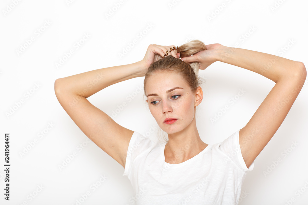 A young, thoughtful lady brushed her blond long hair back to gather it in a bun. A young, thoughtful lady brushed her blond long hair back to gather it in a bun.