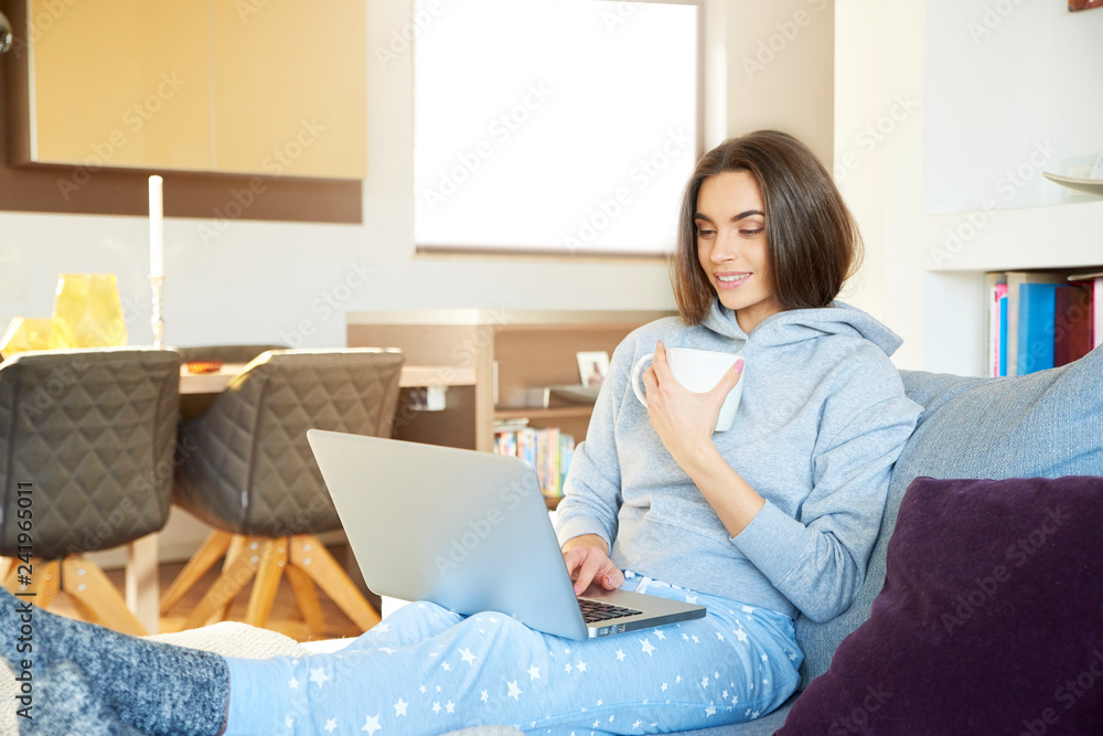 Young woman with her laptop sitting on sofa at home and drinking tea Young woman with her laptop sitting on sofa at home and drinking tea