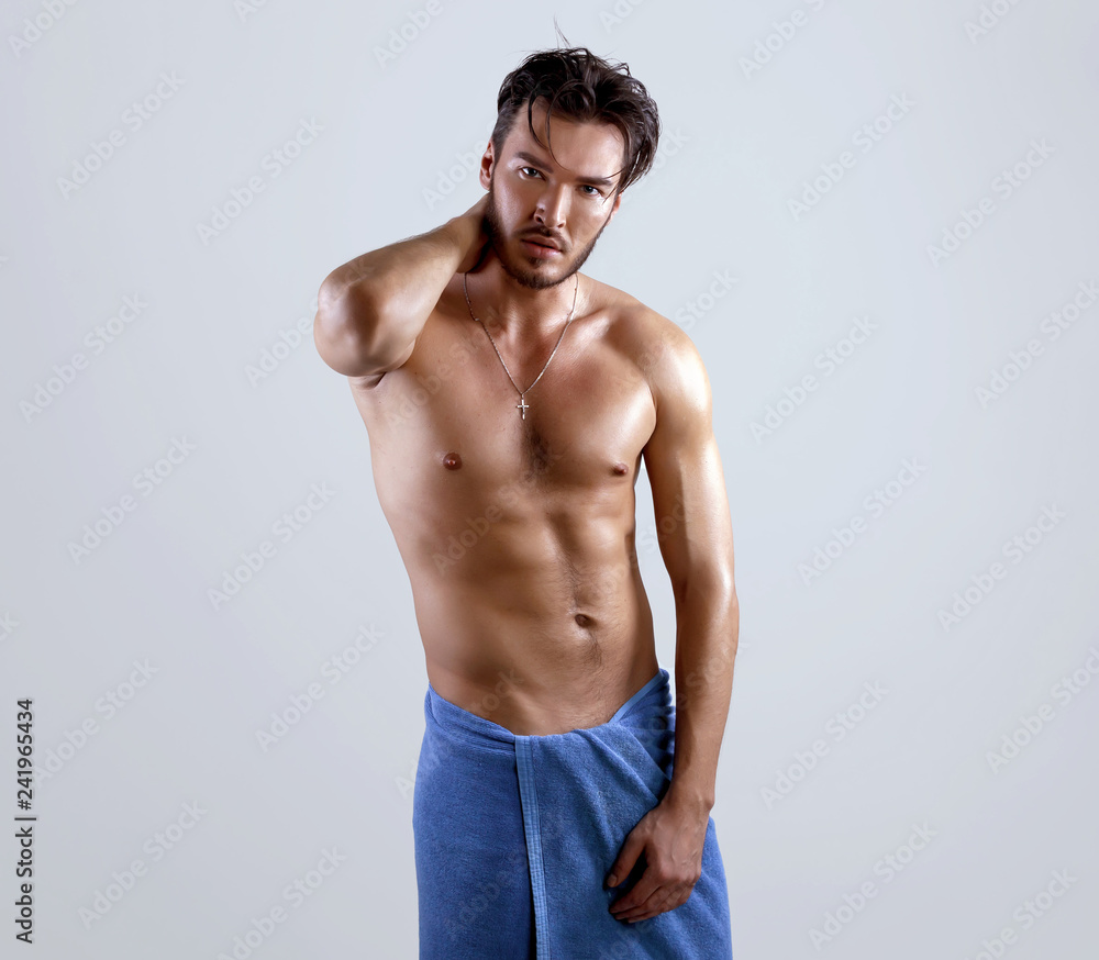 Wet sexy torso handsome men in good shape wrapped in the blue towel and style haircut poses over grey background