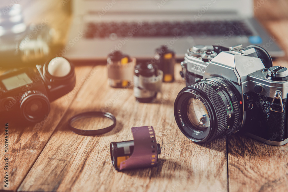 Analog camera, film rolls and vintage photography accessories along with modern equipment and laptop.