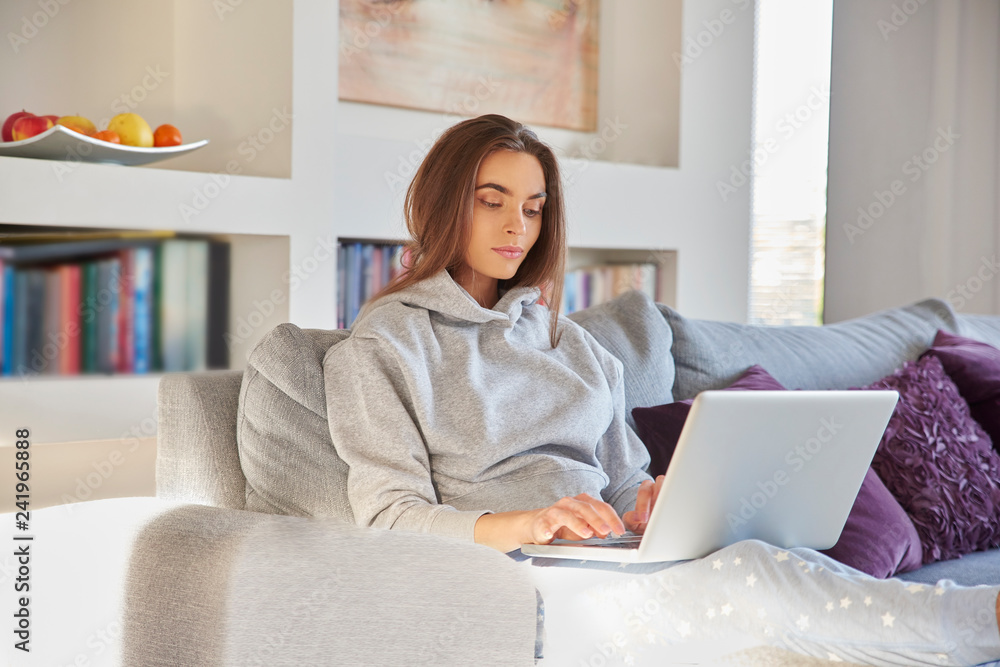 Beautiful young woman relaxing at home and using her laptop Beautiful young woman relaxing at home and using her laptop