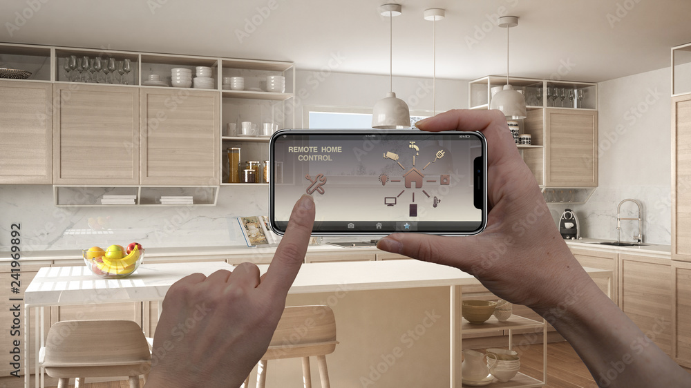 Remote home control system on a digital smart phone tablet. Device with app icons. Interior of minimalist white and wooden kitchen in the background, architecture design Remote home control system on a digital smart phone tablet. Device with app icons. Interior of minimalist white and wooden kitchen in the background, architecture design