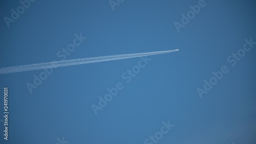 Plane flying on a blue sky, condensation line.