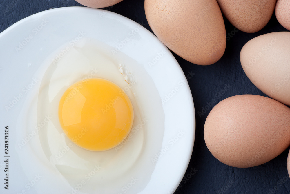 Raw egg guinea fowl in a white plate on a blue background Raw egg guinea fowl in a white plate on a blue background