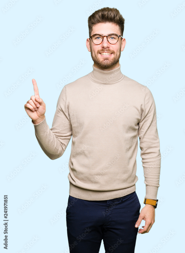 Young handsome business man wearing glasses showing and pointing up with finger number one while smiling confident and happy. Young handsome business man wearing glasses showing and pointing up with finger number one while smiling confident and happy.