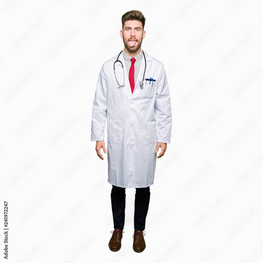 Young handsome doctor man wearing medical coat sticking tongue out happy with funny expression. Emotion concept. Young handsome doctor man wearing medical coat sticking tongue out happy with funny expression. Emotion concept.