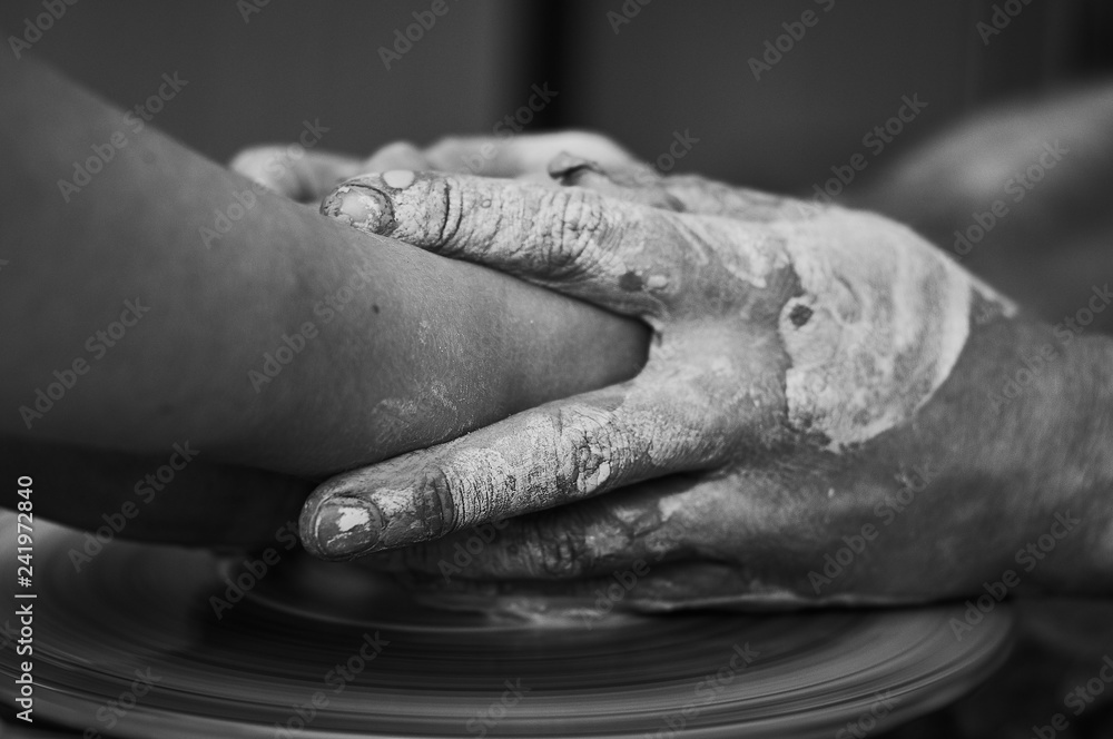 Black and white A man teaches a girl to make clay products on a potter's wheel. Hands close up. Black and white A man teaches a girl to make clay products on a potter's wheel. Hands close up.