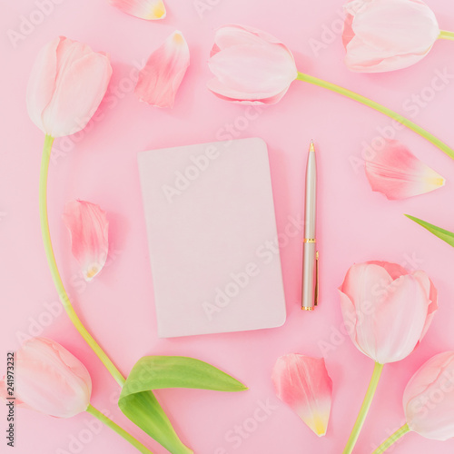 White flowers and petals with notebook and pen on pink background. Female blogger concept. Flat lay, top view.