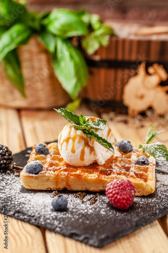 Belgian waffles with a scoop of ice cream, fresh berries raspberries, blackberries, blueberries and mint. Dusted with icing sugar and poured over caramel sauce. selective focus