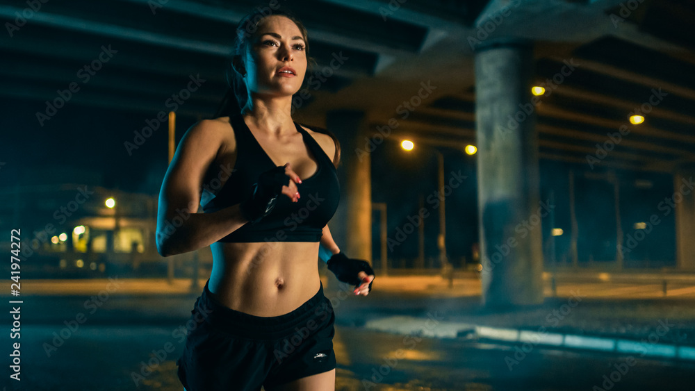 Beautiful Busty Fitness Girl in Black Athletic Top and Shorts is Jogging on  the Street. She is Doing a Workout in a Night Urban Environment Under a  Bridge. Stock Photo