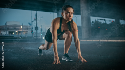 Beautiful Strong Fitness Girl in Black Athletic Top and Shorts Ready for Sprinting. She is Training in an Urban Environment Under a Bridge with Cars in the Background.