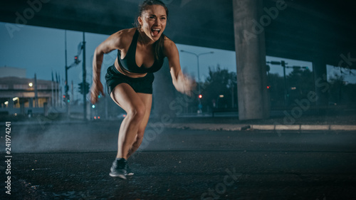 Fototapeta Naklejka Na Ścianę i Meble -  Beautiful Strong Fitness Girl in Black Athletic Top and Shorts Starts Sprinting. She is Running in an Urban Environment Under a Bridge with Cars in the Background.
