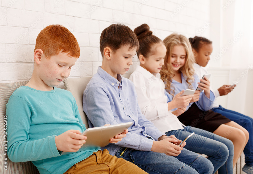 Schoolchildren with modern devices near brick wall Schoolchildren with modern devices near brick wall