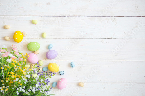 Easter eggs with flowers on white rustic wooden background. View from above