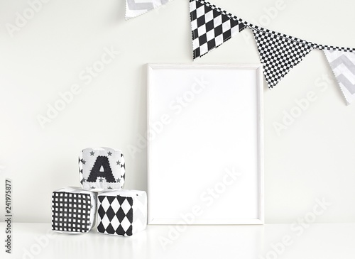 Empty white frame mockup for artwork, painting, posters or photo, monochrome nusery interior with blank frame, flags bunting and soft baby blocks. photo