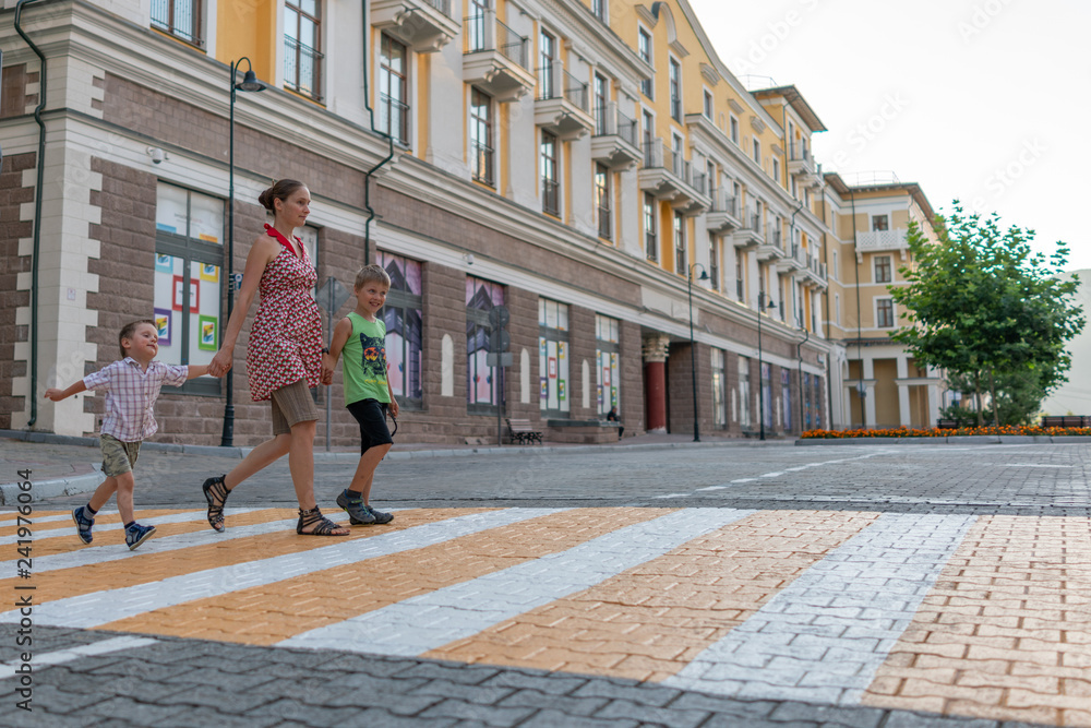 Mom and her two children cross the road at a pedestrian crossing in the summer in a European town