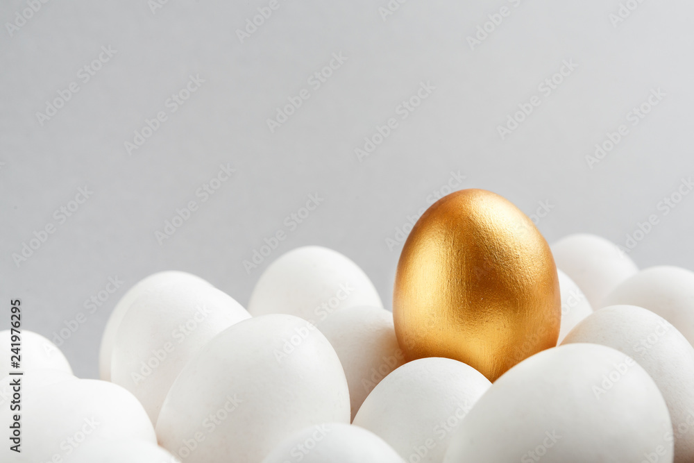 One golden egg among white eggs on gray background. - obrazy, fototapety, plakaty 