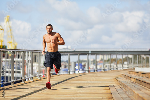 Fototapeta Naklejka Na Ścianę i Meble -  Athletic shirtles man running in urban scene during summer