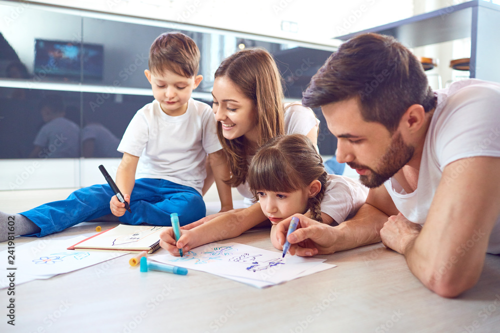A family draws on paper lying on their free time on the floor. A family draws on paper lying on their free time on the floor.