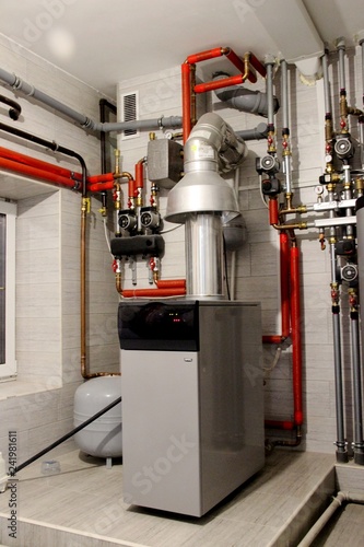 Heating of the house with a large number of steel pipes, pressure gauges and metal pipes, selective focus. Boiler and pipes of the heating system of the house.