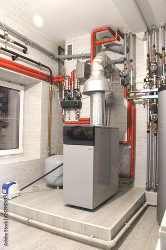 Heating of the house with a large number of steel pipes, pressure gauges and metal pipes, selective focus. Boiler and pipes of the heating system of the house.