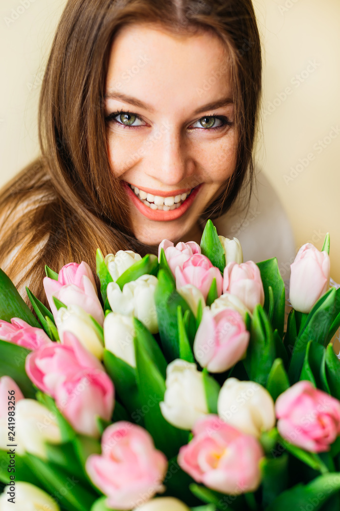 Portrait of a cheerful young blonde woman with big green eyes holding tulips bouquet.