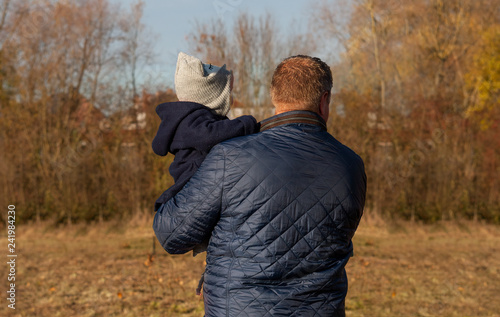 Father carrying young child on his arm against a nature background in the Autumn