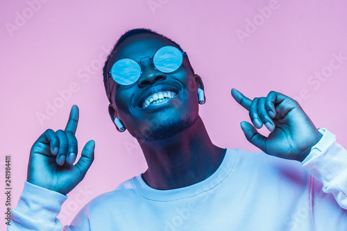 Young smiling african american man listening to music with earphones, dancing isolated on pink background