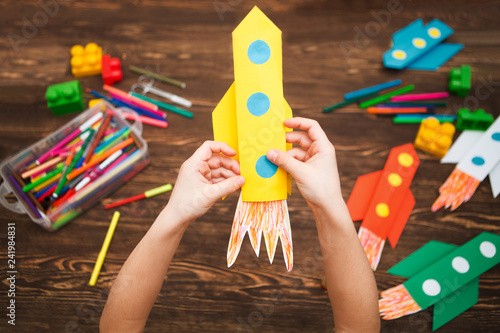 preschool Child in creativity in the home. Happy kid makes rockets from paper. Children's creativity. Creative children play with craft. Tools and materials for children's art creativity on table.