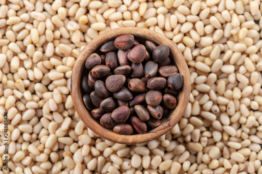 Pine nuts in a round wooden bowl on a background of peeled pine nuts. Pine nuts in a round wooden bowl on a background of peeled pine nuts.