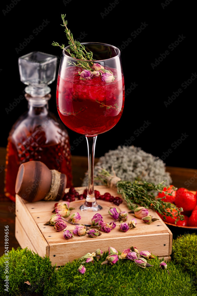 Vertical image of glass with wine alcohol cocktail decorated with cranberry, rosemary and rose flowers at wooden table background.