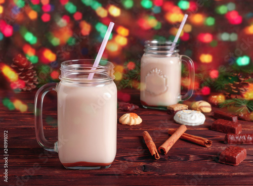 Two glass cups of hot cocoa with milk, cinnamon, candies and straw tube