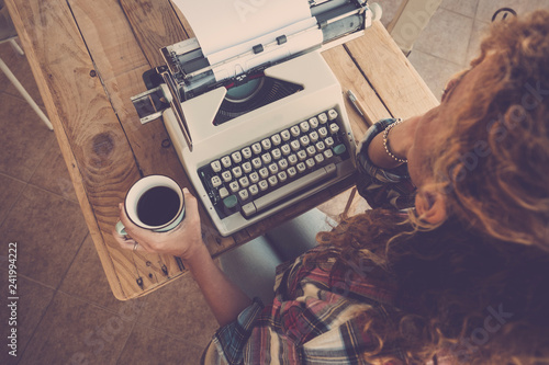 Above view of curly woman thinking and taking coffee with old typewriter on the table ready to write a book or a message in past way - alternative artistic work for independent modern strong lady photo