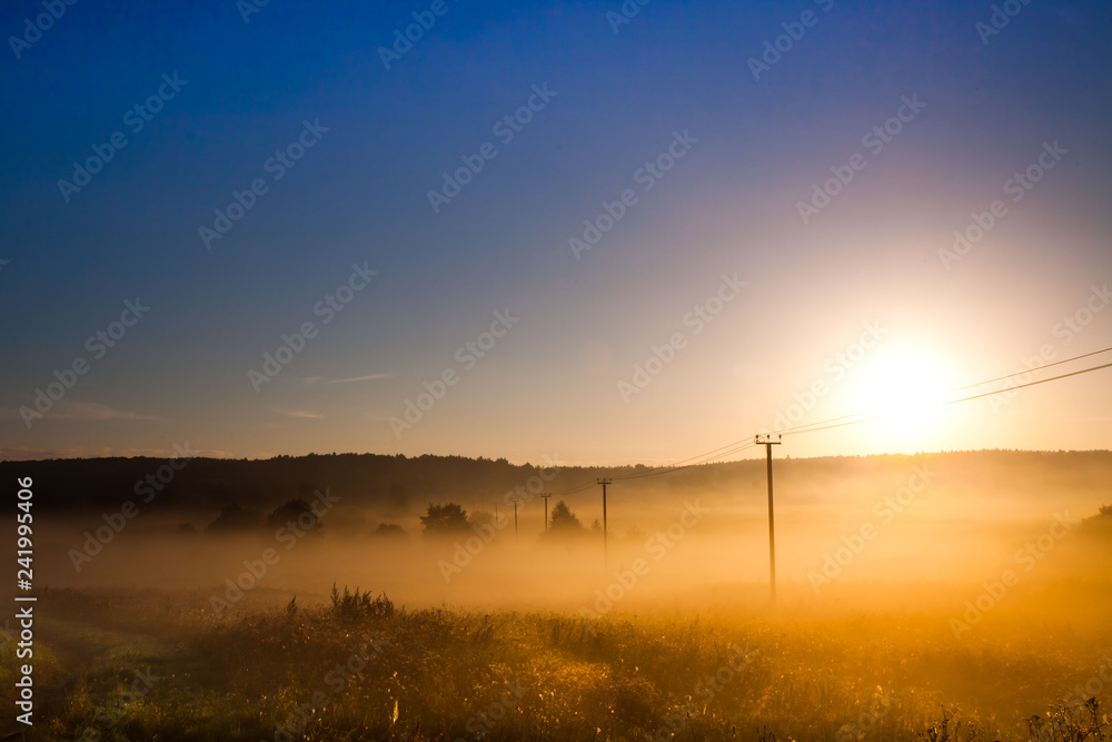 Dawn, the morning sun rises over the field and power transmission line, misty dawn landscape