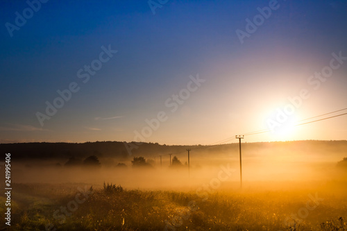 Dawn, the morning sun rises over the field and power transmission line, misty dawn landscape