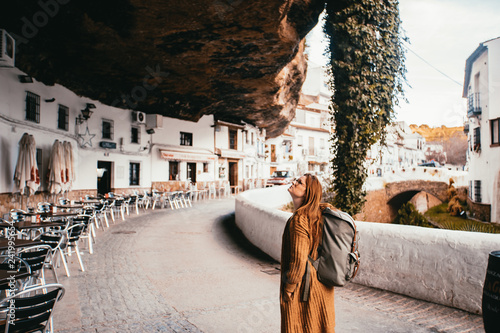 Young female tourist with a backpack is locking above in a small spain village that is build into a rock.