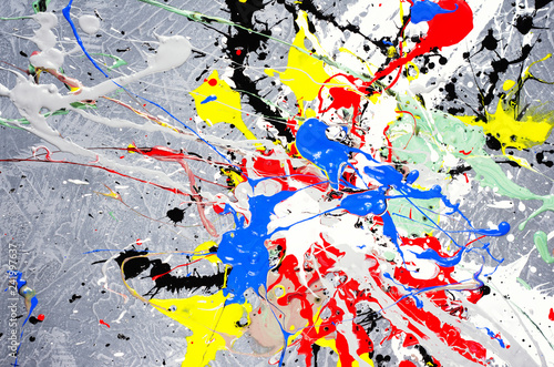 a spot of white and black and yellow and green and red and blue spilled paint on a concrete textured surface