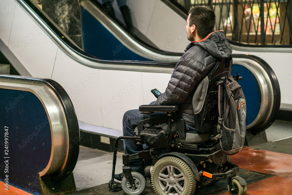 Rear View Of A Disabled Man On Wheelchair In Front Of escalators Rear View Of A Disabled Man On Wheelchair In Front Of escalators