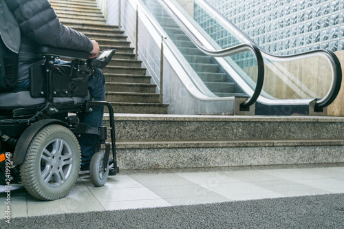 Closeup photo of man on a wheelchair in front of escalators and staircase with copy space