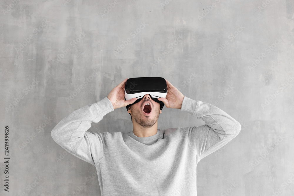 Amazed young man playing video games in VR goggles or 3d glasses, wearing virtual reality headset for on his head
