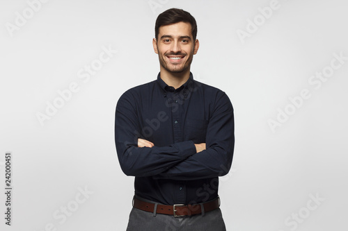 Modern businessman in deep blue shirt standing with crossed arms, isolated on gray background photo