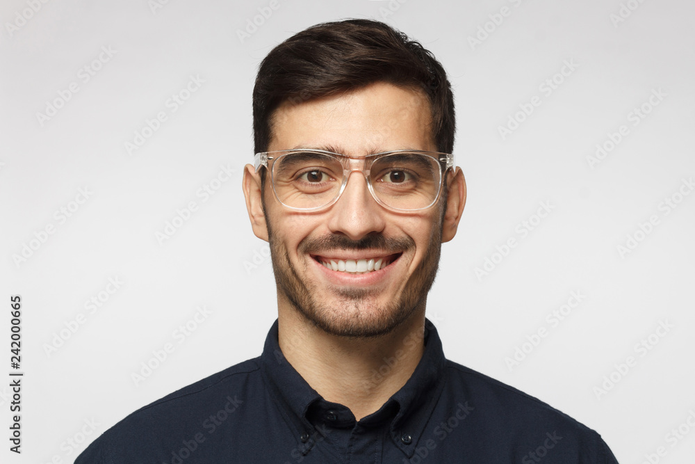 Close-up of young businessman isolated on gray background, smiling with confidence, feeling relaxed and ready for future success Close-up of young businessman isolated on gray background, smiling with confidence, feeling relaxed and ready for future success