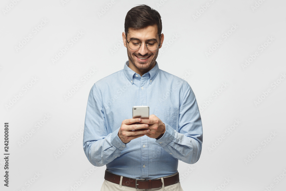 Portrait of cheerful businessman in round glasses typing sms with smart phone, isolated on gray background Portrait of cheerful businessman in round glasses typing sms with smart phone, isolated on gray background