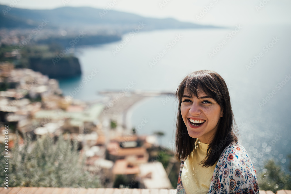 Happy woman traveler smiling at italian coast view.Woman traveling to European south coast.Enoying sunny weather medditerranean seaside