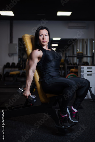 fitness girl trains biceps with dumbbells in the gym.