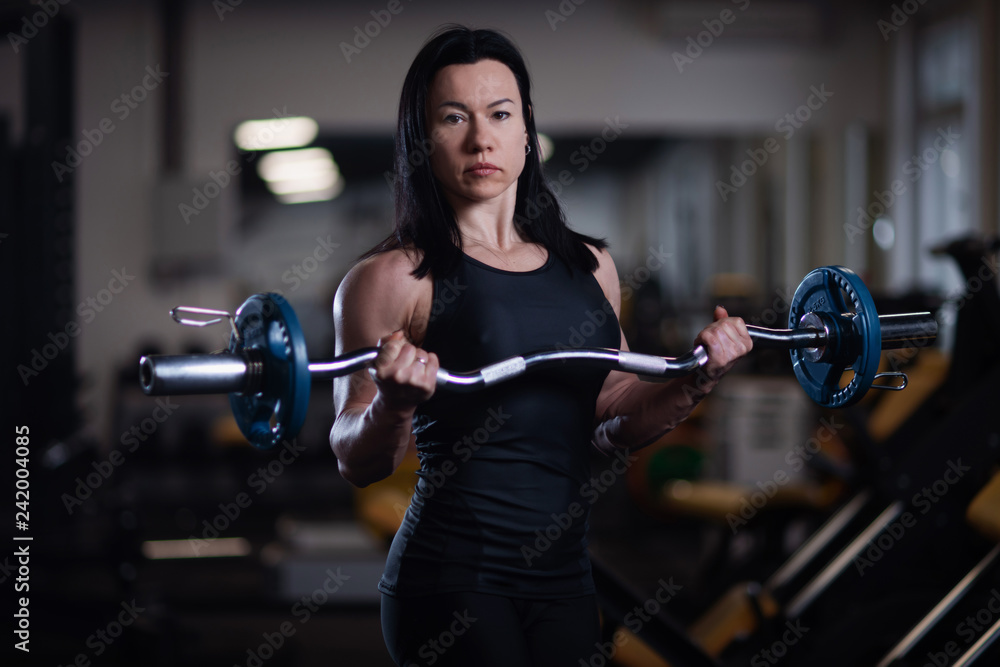 fitness girl trains biceps with barbell in the gym.