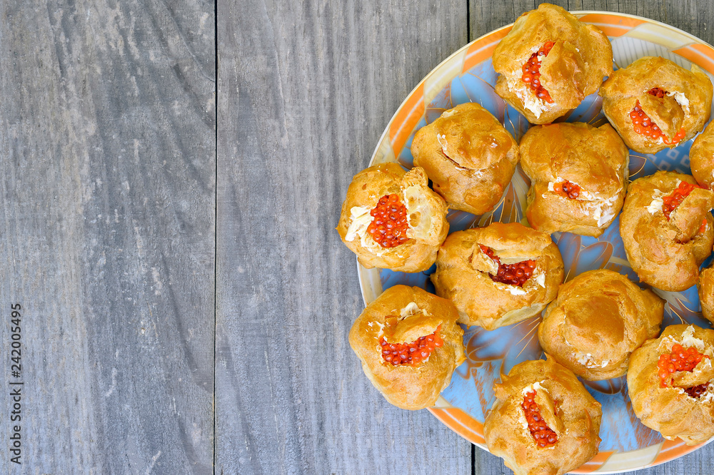 Eclairs with red caviar are laid out on a colored plate on a wooden rustic vintage background. Background, copy space Eclairs with red caviar are laid out on a colored plate on a wooden rustic vintage background. Background, copy space